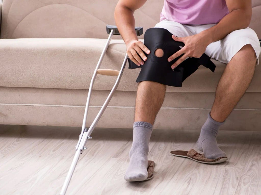 Injured man with crutches and a knee brace sitting on a couch, representing how trusted personal injury lawyers at Thompson Law help injury victims recover compensation.