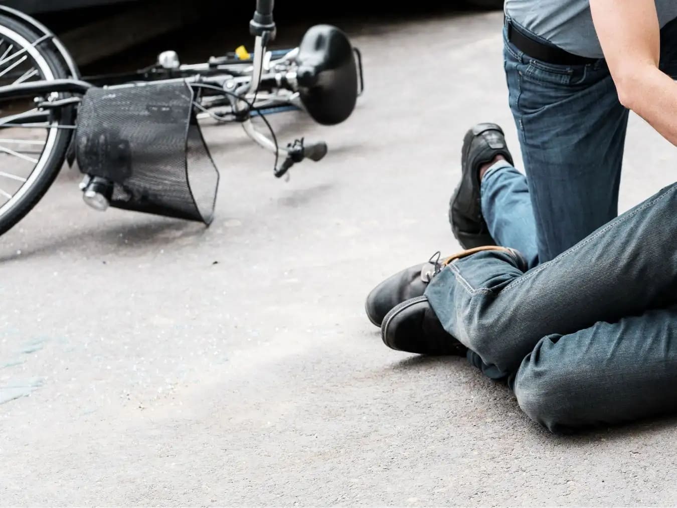 Person kneeling on the ground next to a fallen bicycle on a paved surface.