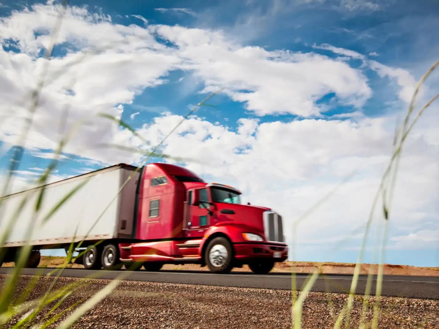 Red semi-truck with a trailer driving on an open highway under a cloudy sky.