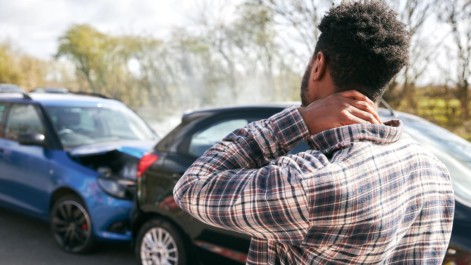 Driver holding neck after a car accident while standing near damaged vehicles