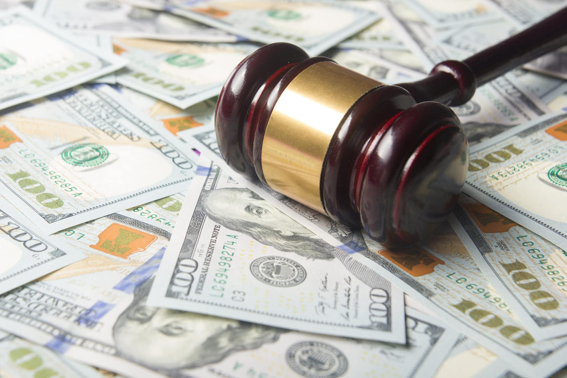 Wooden gavel with a gold band resting on a spread of hundred dollar bills.