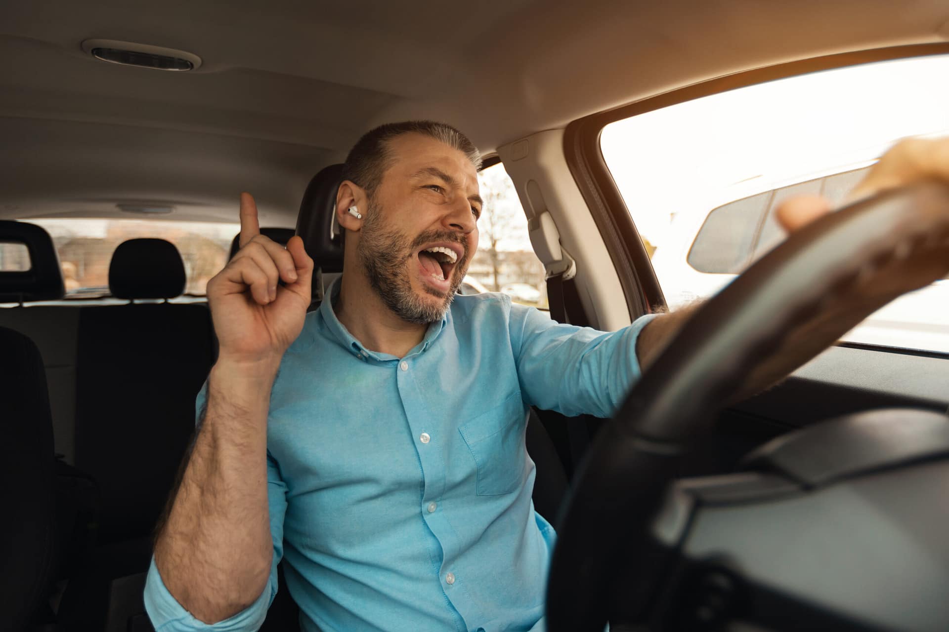 Hombre feliz con audifonos or auriculares disfrutando de la música conduciendo un coche de lujo