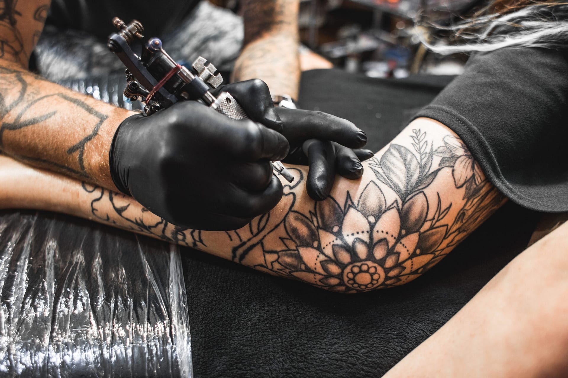 Get a tattoo - girl with dreadlocks in a tattoo parlor. The master creates a picture on the body of a young beautiful girl. Close-up of hands and tattoo machine