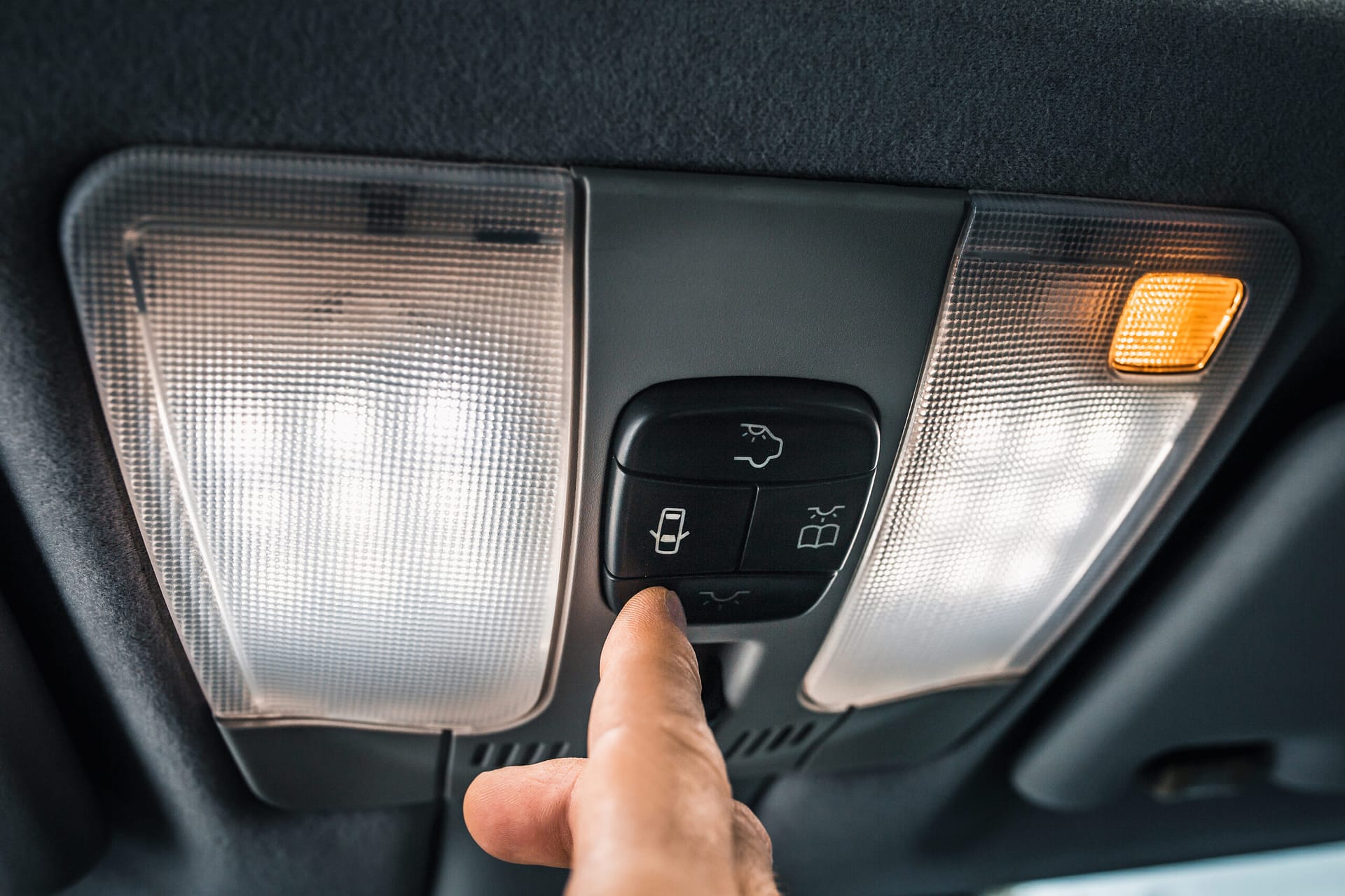 Driver pressing interior controls on a car ceiling panel