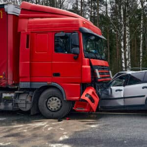 Red 18-wheeler semi truck crashed into a gray car on a roadway