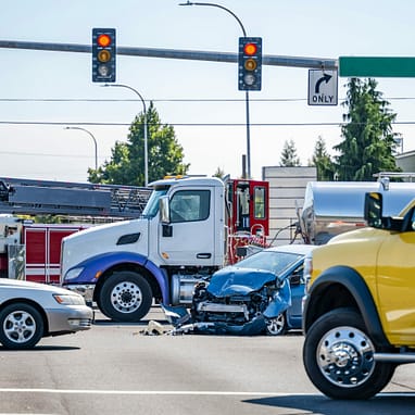 The Differences Between Truck Accident and Car Wreck Claims 2 Damaged cars after a car accident crash involving a big rig semi truck with semi trailer at a city street crossroad intersection with traffic light and rescue services to help the injured