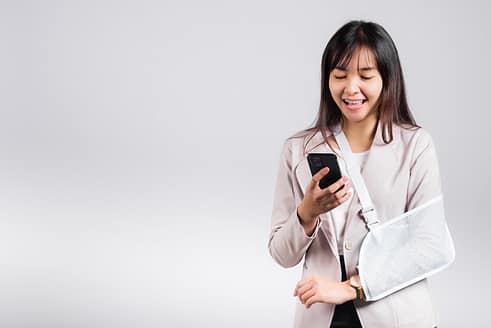 Personal Injury Social Media Guidelines 2 Woman confident smiling broken arm after accident and wear arm splint for treatment and hold smartphone, happy Asian female sling supported hand isolated on white background, social media, copy space.