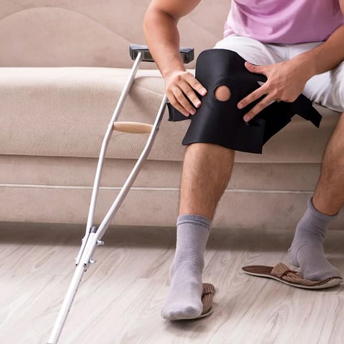 Person sitting on a couch with a knee injury and crutches