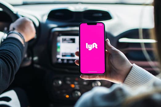 Una chica dentro de un coche sostiene un teléfono inteligente con la aplicación Lyft en la pantalla. Acuerdos de conciliación y cláusulas de confidencialidad de Lyft. Acuerdo de Lyft.