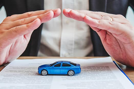 Hands hovering protectively over a toy car on top of an insurance document