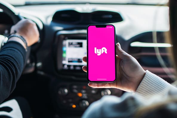 Chica dentro del coche sosteniendo un teléfono inteligente con la aplicación Lyft en la pantalla.