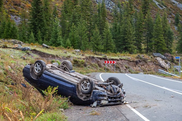 Car accident place on a bend, overturned car lies on the roof, broken bumper, glass, mountain road background, horizontal, copy space- Ontario Car Accident Lawyers
