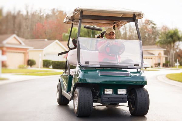Active senior man driving a golf cart on a neighborhood road. Golf carts on roadways by state; what's the law?