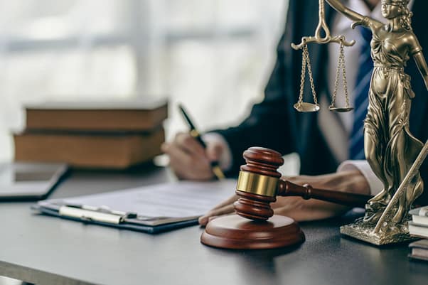 Man sitting at a desk reviewing paperwork with Lady Justice on the table next to a gavel.