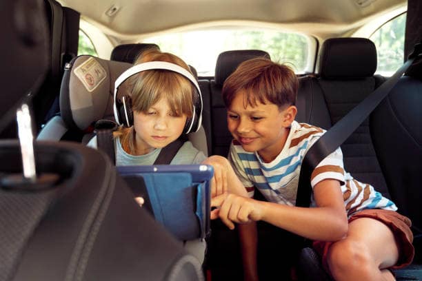 Two children sitting in the back seat of a car wearing seat belts