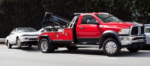 Surprise! Your car is G-O-N-E! Red tow truck hauling away white car that is being towed away