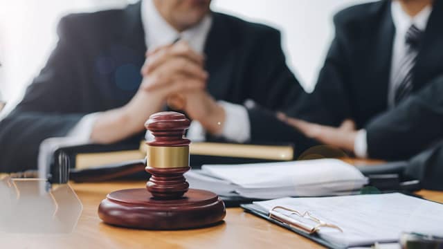 Two people in business attire sitting across from each other at a desk with a wooden gavel and documents in the foreground.