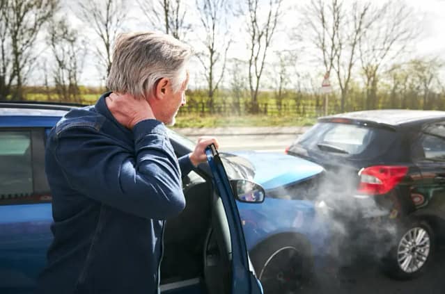 Atlanta Personal Injury Lawyer: What to Know Before You File a Claim in Georgia 2 Man standing next to a car holding the back of his neck after a collision, with steam rising from a damaged vehicle in the background.