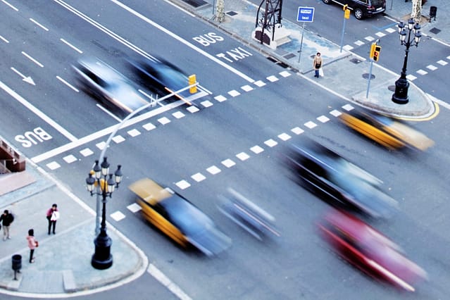 Aerial view of cars in motion crossing a busy city intersection with pedestrians on the crosswalk