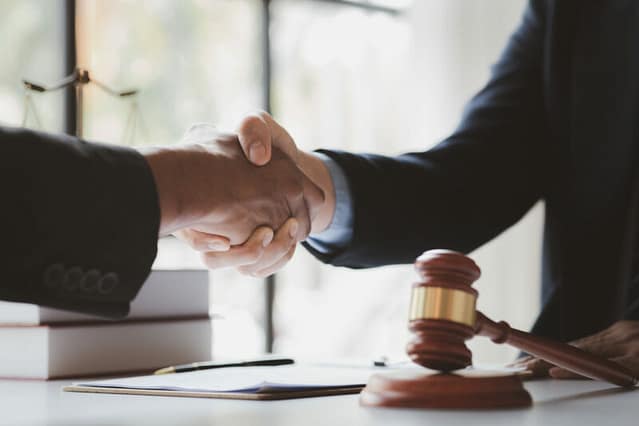 Client shaking hands with an attorney at a desk with a gavel in the foreground