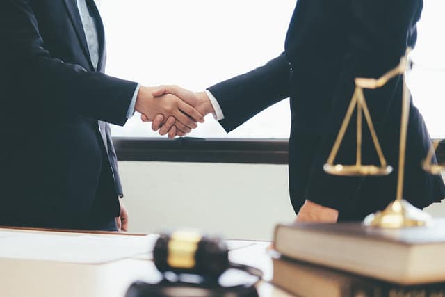 Two people shaking hands in a law office with a gavel and scale of justice on the desk