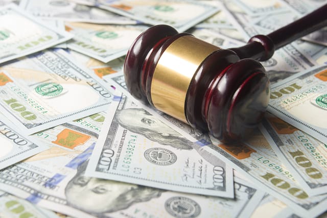 Wooden gavel with a gold band resting on a spread of hundred dollar bills.