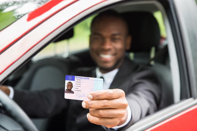 Happy Young African Businessman Showing His Driver License From Open Car Window - The Penalties for Driving Without a License in Texas