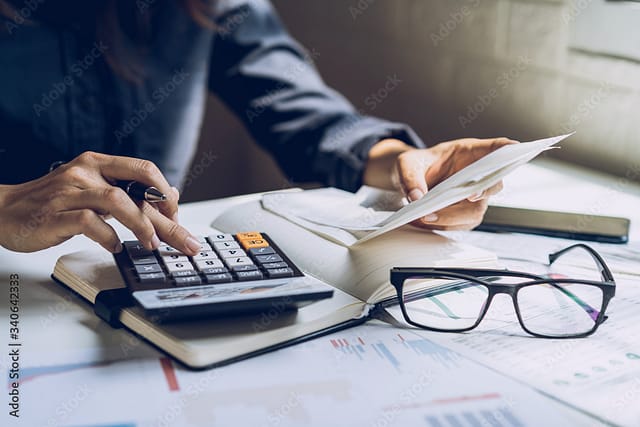 Person using a calculator while reviewing documents and financial papers on a desk.