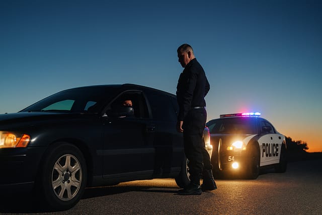 Police officer conducting a traffic stop at night with patrol car lights in the background