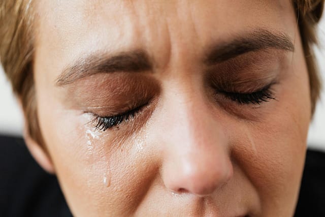 Close-up of a person with eyes closed and tears running down their face.