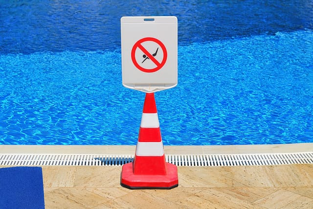 Red and white safety cone with a no diving prohibition sign placed on the edge of a swimming pool.