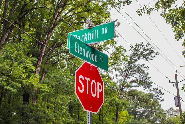 Stop sign and street signs at a residential intersection surrounded by trees