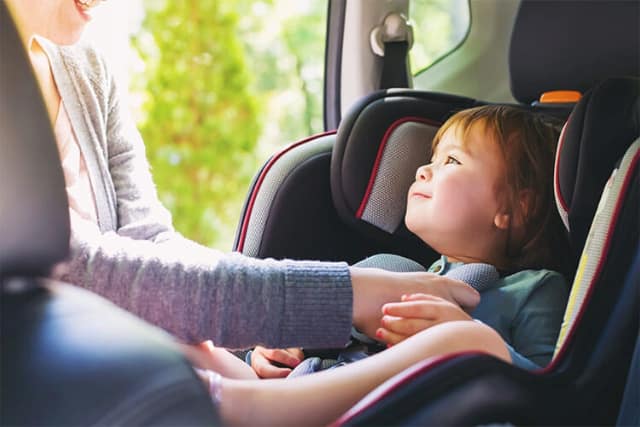 Child sitting in a safety seat while an adult adjusts the harness inside a car