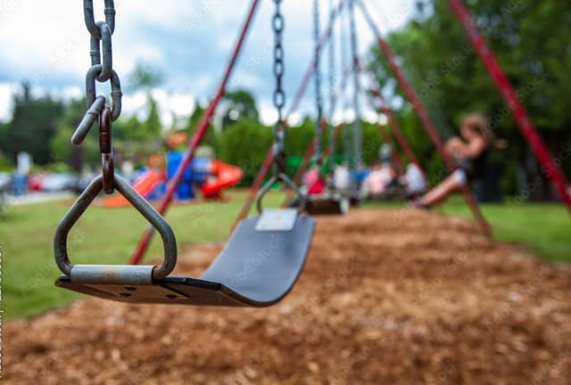 Playground swing with children playing in the background, illustrating the question of who is liable if my child is injured on a playground.