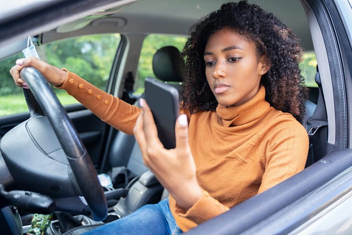 Una adolescente conduciendo un coche distraída por su teléfono móvil