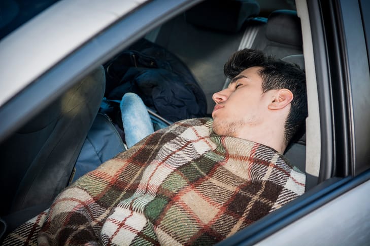 Joven apuesto durmiendo dentro de su auto, exhausto, cansado. ¿Es ilegal dormir en tu carro o vivir fuera de su automóvil en Texas?