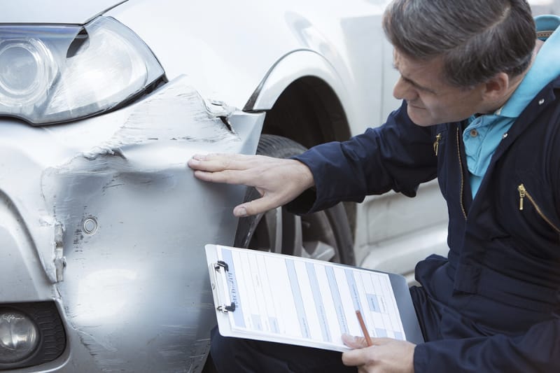Man looking at damage to the bumper of a car.