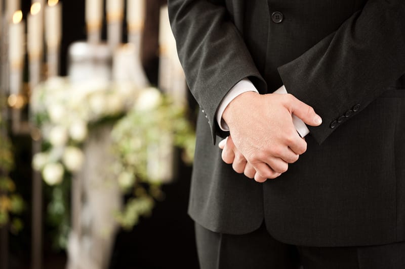 Religion, death and dolor - undertaker at funeral standing in front or urn. Baytown Wrongful Death Lawyers
