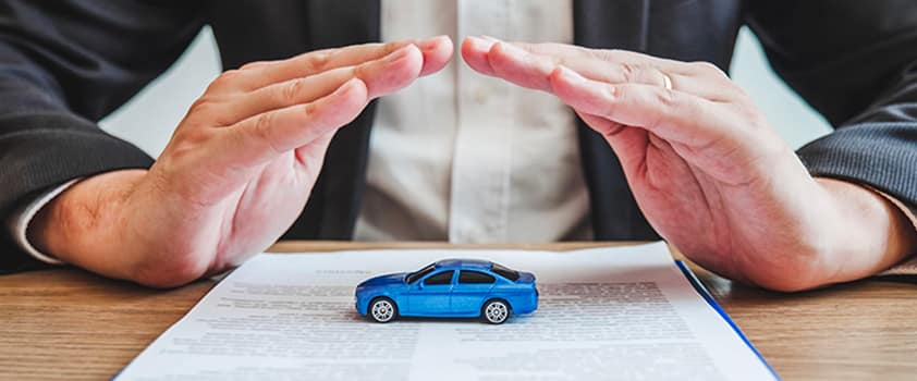 Hands hovering protectively over a toy car on top of an insurance document